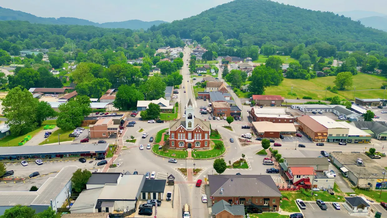 Drone view looking straight up the main street through downtown Blairsville, with the courthouse on its circular square in the center and green mountains beyond.