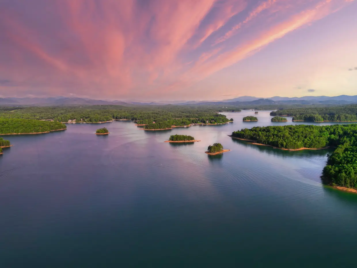 Drone view of Lake Nottely at sunset, with pink streaked clouds reflected in calm water dotted with small wooded islands and distant mountains.