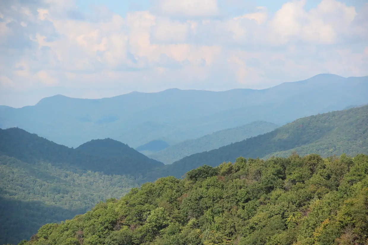 Layered blue-green mountain ridges receding into haze, with forested Locust Log Ridge in the foreground and Brasstown Bald on the far horizon.