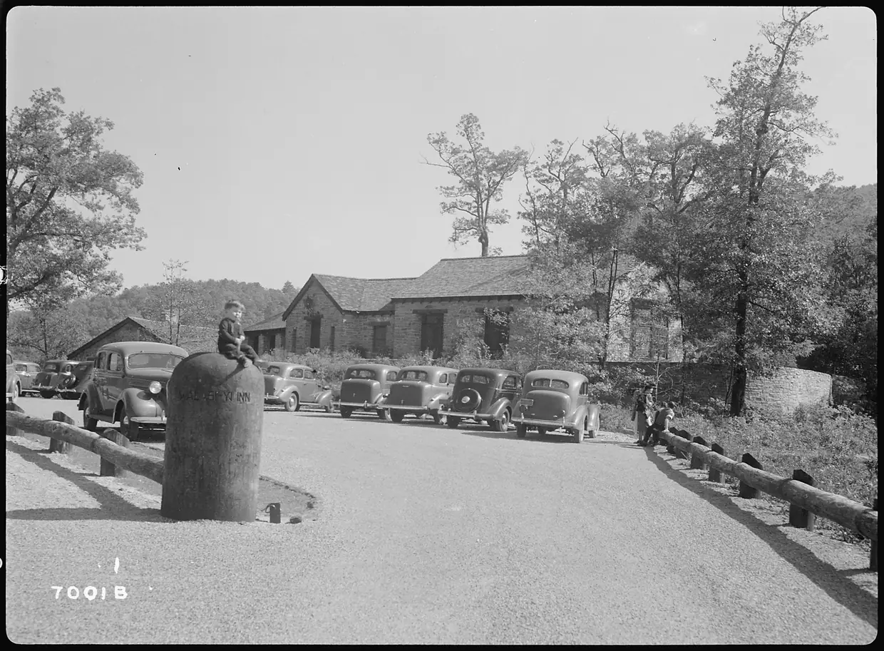 Black-and-white 1939 photo of the stone public lodge at Neel Gap, with 1930s cars parked along a curving drive and a child sitting on a stone post.