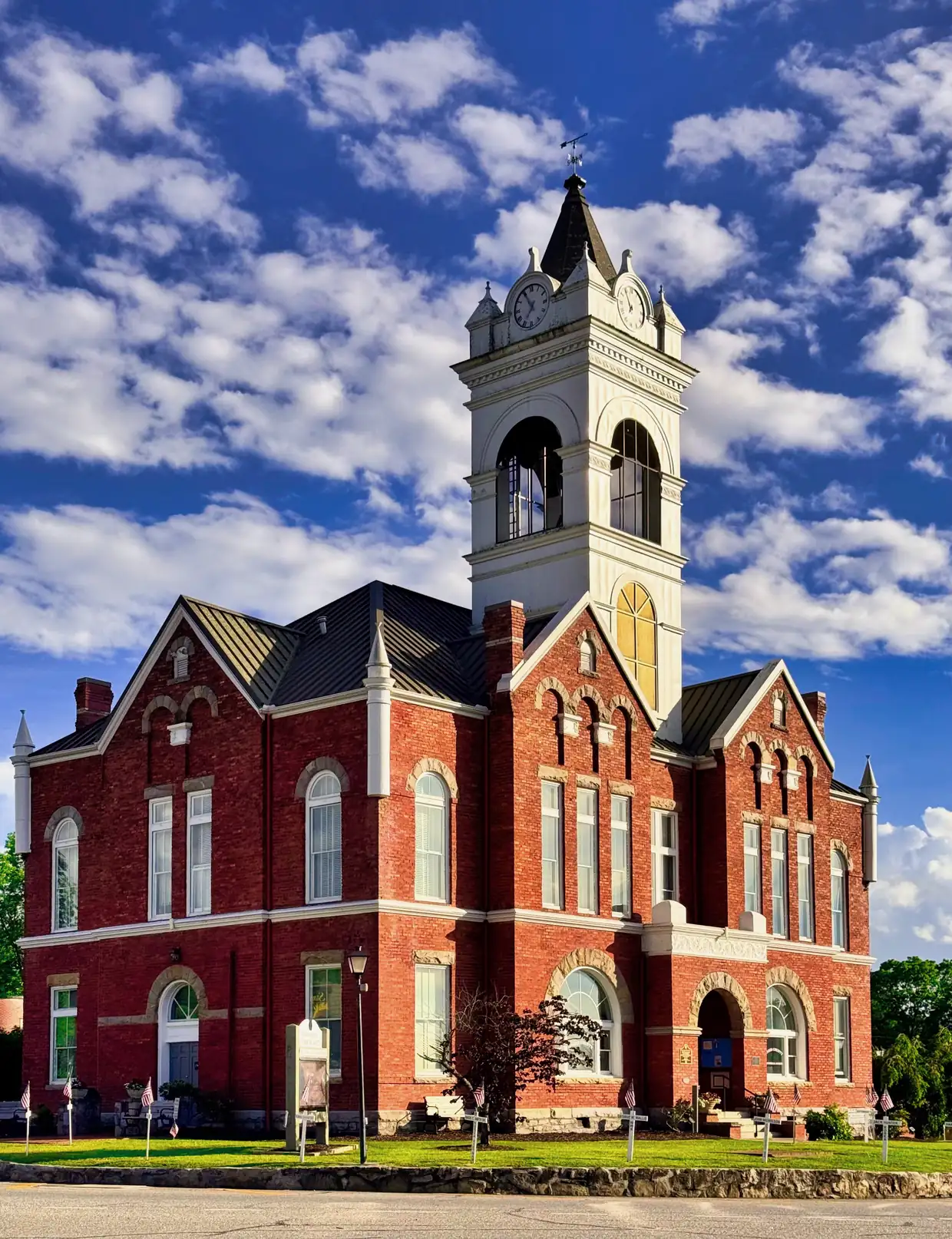 Vertical view of the red-brick Old Union County Courthouse rising to its white clock and bell tower against a vivid blue sky with puffy clouds (heavily color-processed).