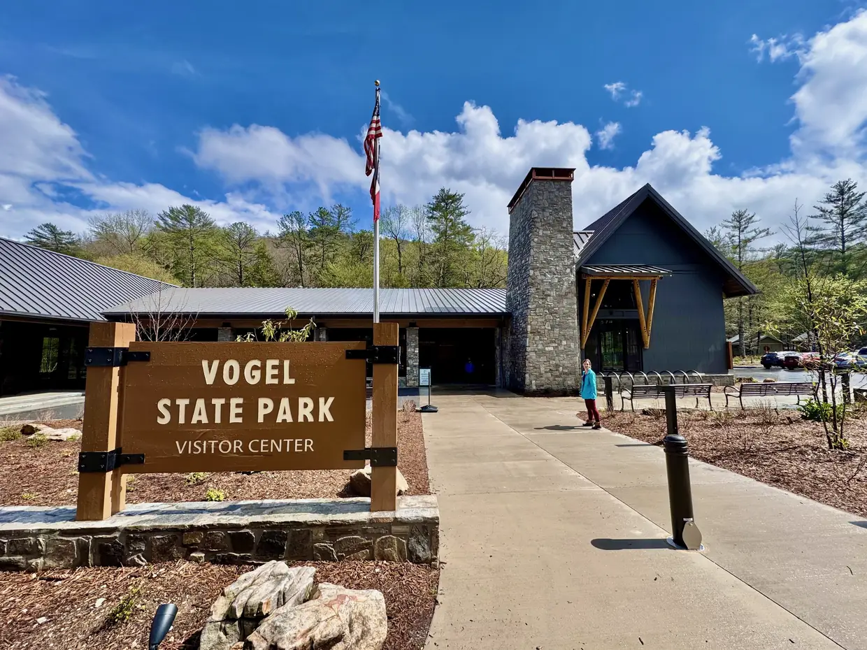 The new Vogel State Park visitor center with a wooden 'Vogel State Park Visitor Center' sign, stone chimney, flagpole and walkway under a blue sky.