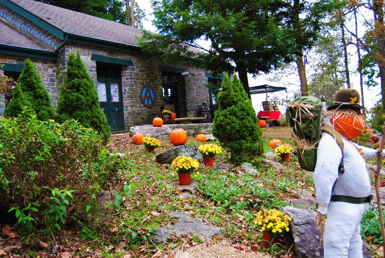 The stone Walasi-Yi building decorated for fall with pumpkins, potted mums and a scarecrow hiker wearing a backpack.